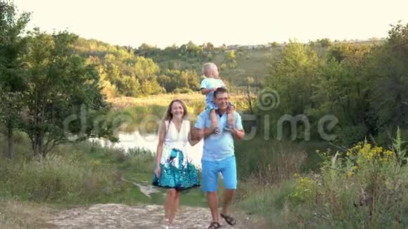 在一个夏天的日落时分爸爸妈妈带着一个小儿子在公园里的河边散步聊天视频的预览图
