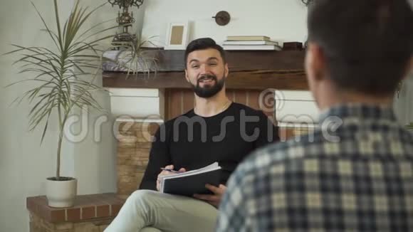 成年白种人坐在报纸上说话微笑专业男性心理学家给病人讲故事视频的预览图