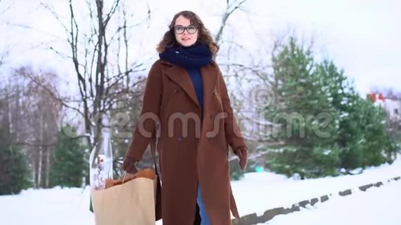 穿着针织围巾站在公园里拿着购物袋的年轻美女视频的预览图