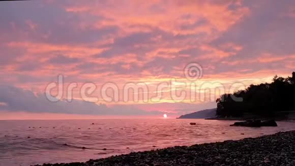 大海卵石海滩上的红色日落视频的预览图