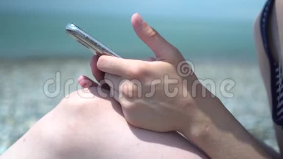 在海岸模糊背景下年轻女性用智能手机特写休息和技术上网冲浪视频的预览图