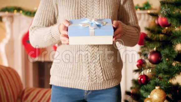 4K镜头年轻女子穿羊毛衫站在圣诞树和壁炉旁边展示圣诞礼物视频的预览图