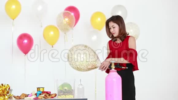 亚洲女人穿着红色衬衫用气球泵吹闪闪发光的气球身后有五颜六色的气球是聚会的概念视频的预览图