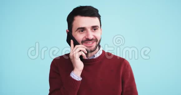 带着蓝色背景墙的摄影棚里一个微笑的非凡的年轻人在镜头前用手机说话视频的预览图