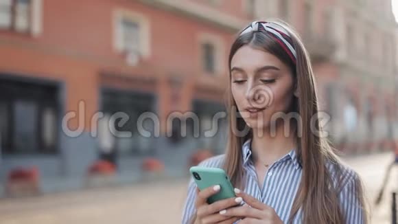 可爱的女人穿着蓝色和白色条纹连衣裙使用智能手机上的应用程序在旧城街道上行走美丽美丽视频的预览图