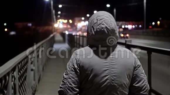 一个穿灰色外套戴着兜帽的女孩晚上在桥上从后面看照相机在动回放缓慢视频的预览图