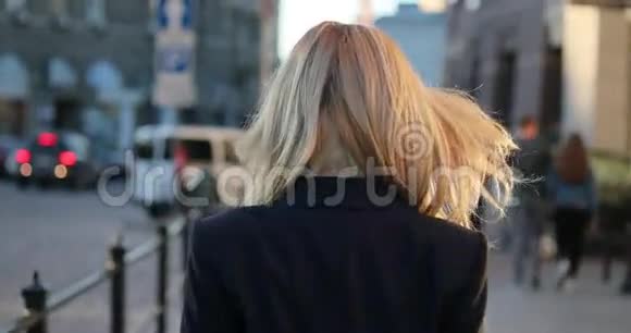 一位身穿正式服装戴着眼镜的金发美女走在城市街道上的后景转向镜头视频的预览图