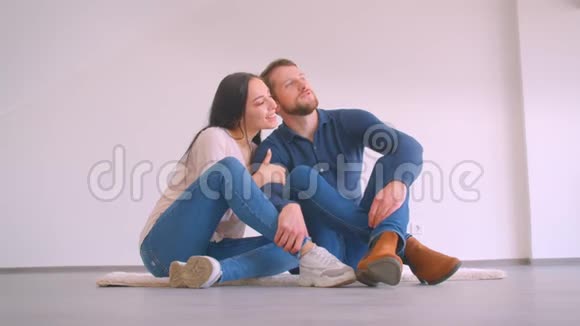 年轻的白种人夫妇坐在新公寓的地板上拥抱和亲吻幸福视频的预览图