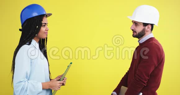 在一个黄色背景墙的工作室里一位建筑师一位非洲裔女士和一位戴着蓝色头盔的工程师视频的预览图