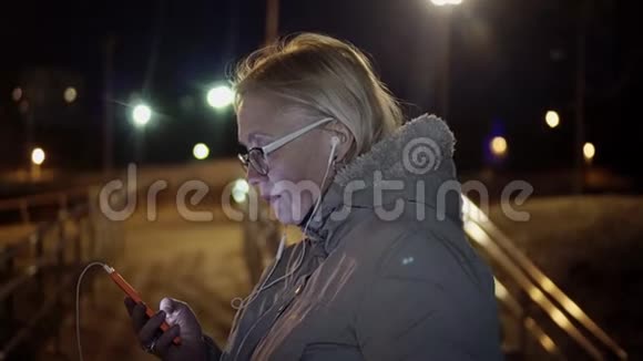 女孩晚上盯着街上的电话安雅戴着白色耳机一阵微风在吹视频的预览图