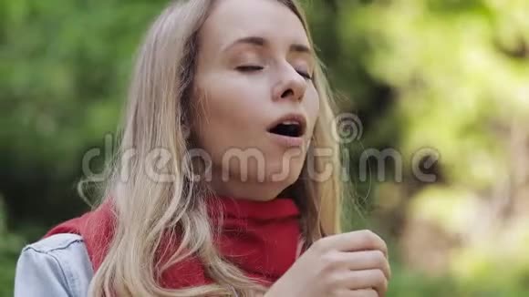 生病的年轻女子戴着红领巾感觉不好喉咙痛站在公园里痛苦的吞咽视频的预览图