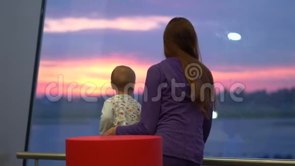 一个年轻的女孩和她的儿子在日出时透过机场的窗户缓慢地看着视频的预览图