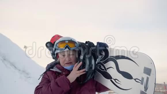 在冬天的度假胜地雪坡上一位年长的妇女扶着滑雪板在肩上行走视频的预览图