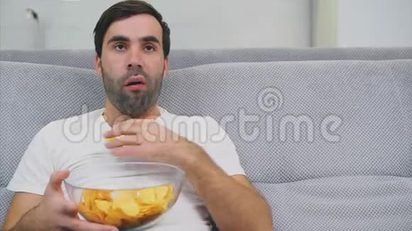穿T恤的家伙坐在沙发上吃薯片看电视手里拿着遥控器视频的预览图