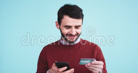 在一个蓝底墙男用手机和信用卡在网上下单的工作室里他非常高兴视频的预览图
