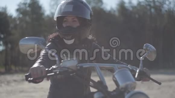 肖像可爱的女人戴着黑色头盔坐在摩托车上看着远处爱好旅游和积极的生活方式视频的预览图
