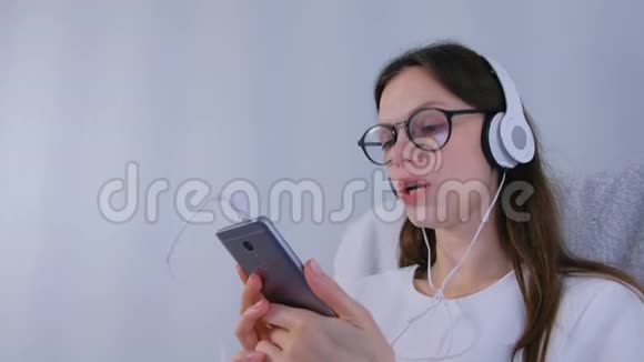 戴眼镜的女人正在智能手机上用耳机听音乐唱一首歌视频的预览图