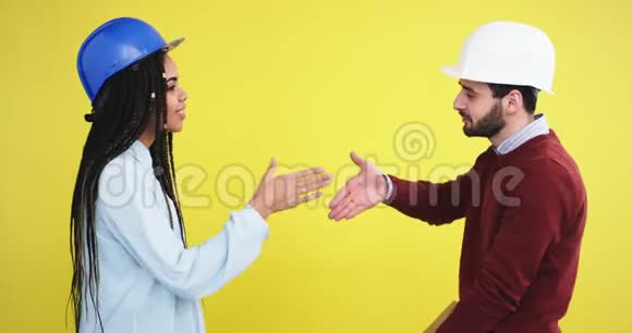 在一个黄色背景墙的工作室里两位建筑师一位非洲女士和一位戴着蓝白头盔的男人视频的预览图