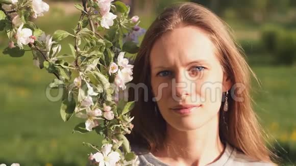 白种人美丽的女孩在一个开花树的背景下看着相机视频的预览图
