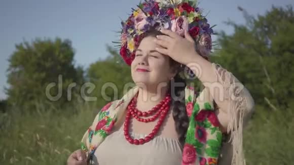 一幅可爱丰满的女人的肖像头上戴着花环在绿色的夏日田野上阳光下微笑连接视频的预览图
