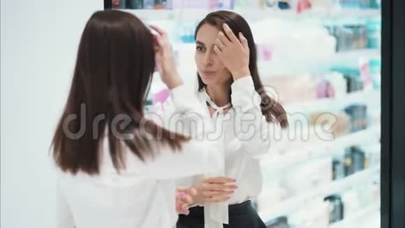 美丽的女孩在化妆品店的镜子前打扮自己慢动作视频的预览图