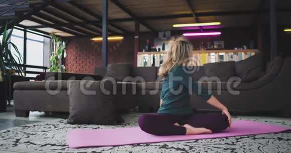 漂亮的金发女人练习瑜伽她早上在瑜伽垫上伸展身体在现代工作室视频的预览图