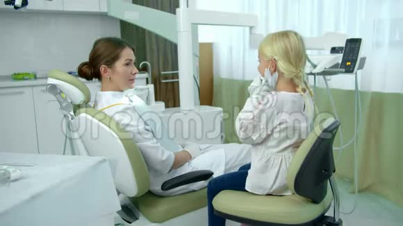 牙医坐在病人的椅子上和女孩说话视频的预览图