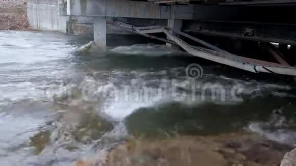 河流在城市里一座有旧管道的桥下视频的预览图