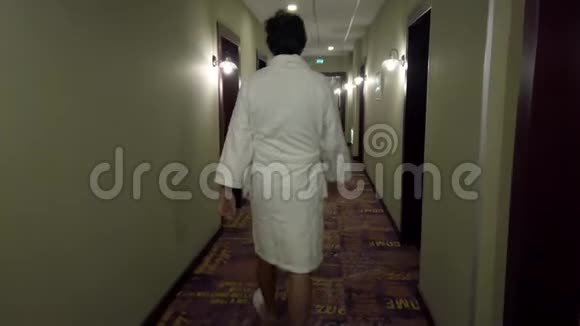 穿着浴袍和拖鞋的男人走在长长的酒店走廊里视频的预览图