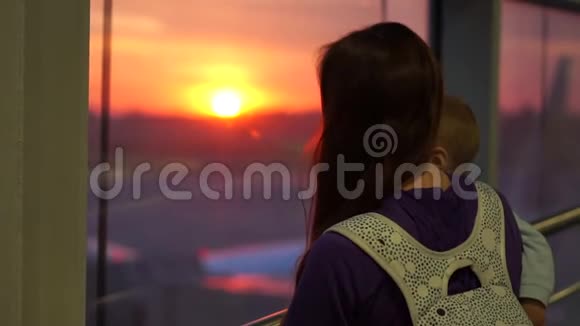 一个女孩带着一个儿子看着机场的窗外日出时动作缓慢视频的预览图