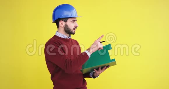 现场负责人在工作室里一个黄色背景墙戴着一个安全的蓝色头盔分析着什么还有一个年轻人视频的预览图