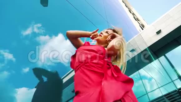性感金发女郎在玻璃建筑映衬天空的低角度舞蹈视频的预览图