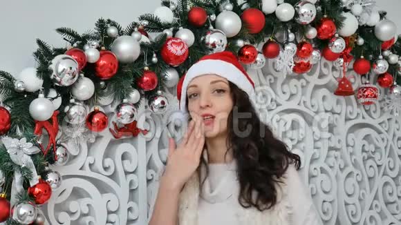 圣诞装饰的摄影棚里戴着红色圣诞帽的快乐女孩在空中接吻视频的预览图