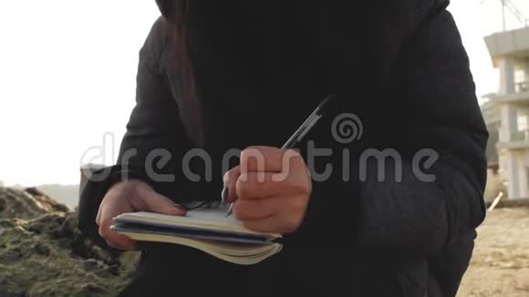 戴着针织帽的海边美女在笔记本上用笔写字视频的预览图