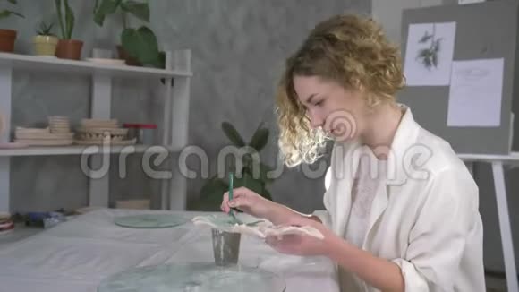 陶工艺术家的肖像妇女在手工工作室用画笔和绿色颜料绘制粘土板视频的预览图