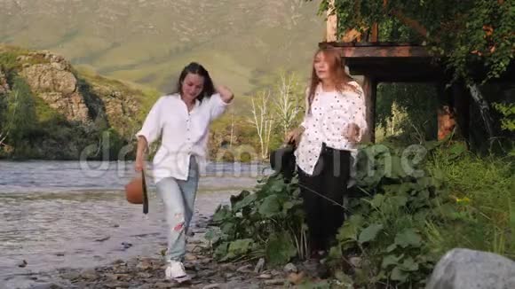 两个女朋友戴着帽子穿着白衬衫在山里在大自然的背景下跳舞女游客跳舞视频的预览图