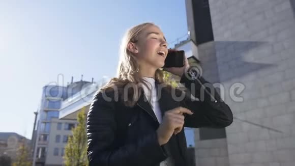 日落时分美丽的年轻女子正走在城市的街道上与她的朋友在智能手机上交谈视频的预览图