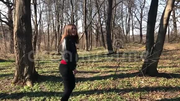 一个穿着黑色皮夹克的可爱女孩穿过树林一个清澈的女孩美丽地微笑着转向照相机视频的预览图