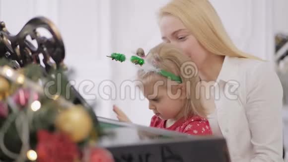 小女孩和她妈妈一起弹钢琴钢琴装饰着新年装饰视频的预览图