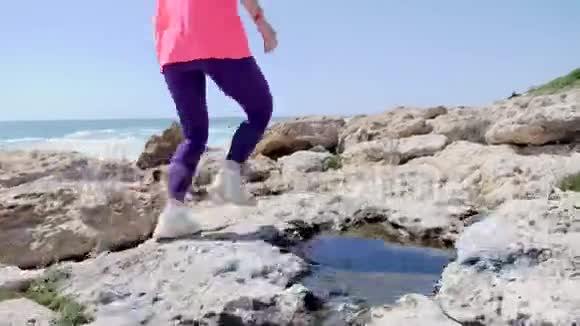 年轻健康的女人沿着海滩经营岩石小径小径在岩石上奔跑慢动作视频的预览图
