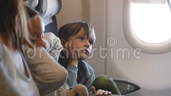 可爱的小男孩很无聊在长假和家人一起飞行时在飞机窗口座位上环顾四周视频的预览图