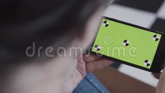黑头发的女少女使用绿色屏幕的智能手机坐在室内库存录像女人拿着手机视频的预览图