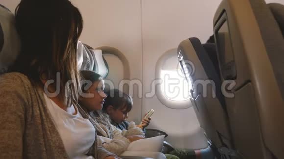 在长时间的飞机飞行中年轻漂亮的母亲和两个无聊的孩子一起去度假视频的预览图