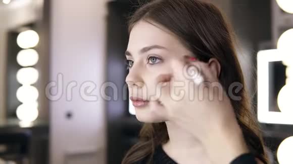 深色头发的女人用化妆刷在颧骨上涂化妆品女孩在沙龙化妆涂上胭脂视频的预览图