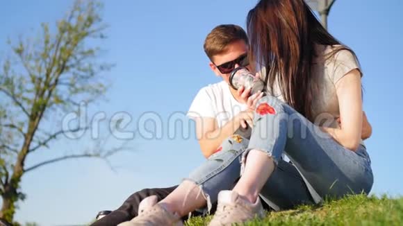 浪漫的一对夫妇喝咖啡坐在靠近池塘的绿草上靠在天空上夫妻信任爱情和幸福视频的预览图