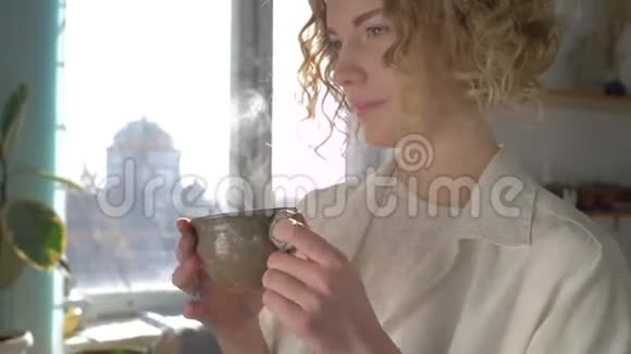 咖啡休息时间快乐微笑画家妇女与杯热饮料享受创意过程阳光明媚的窗户视频的预览图
