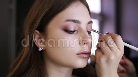 迷人的年轻化妆模特用自然化妆坐在镜子前从侧面看影师的作品视频的预览图