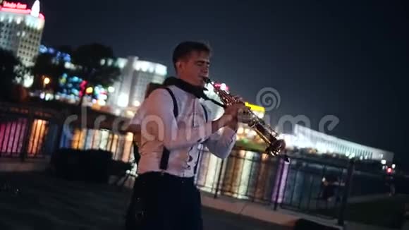 两名街头音乐家一名萨克斯演奏家和一名吉他手在夜城的堤岸上演奏美丽的夜景视频的预览图