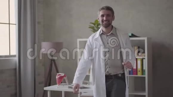 英俊的积极成功和满意的男人穿着白色长袍在现代诊所跳舞快乐医生视频的预览图