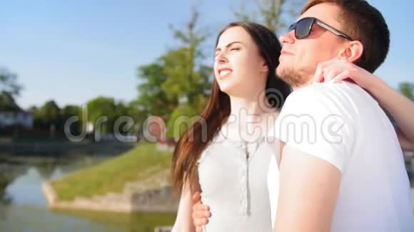 一对年轻快乐的夫妇的肖像在池塘附近的绿色夏季公园里的浪漫情侣一起快乐中弹视频的预览图